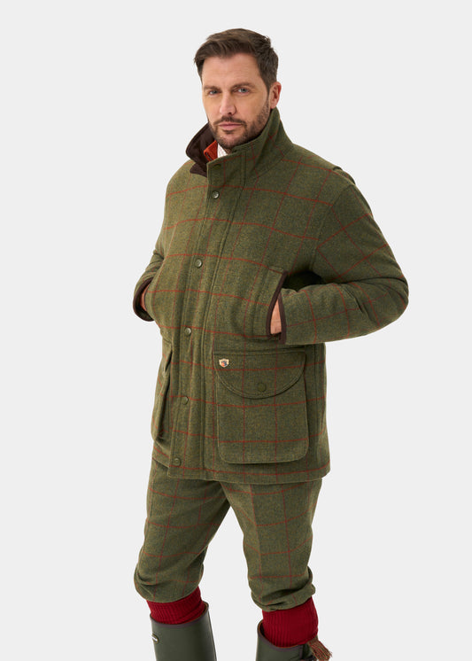 Man wears Combrook Men’s Tweed Waterproof Shooting Field Coat in Reed, hands in pockets, against white background.