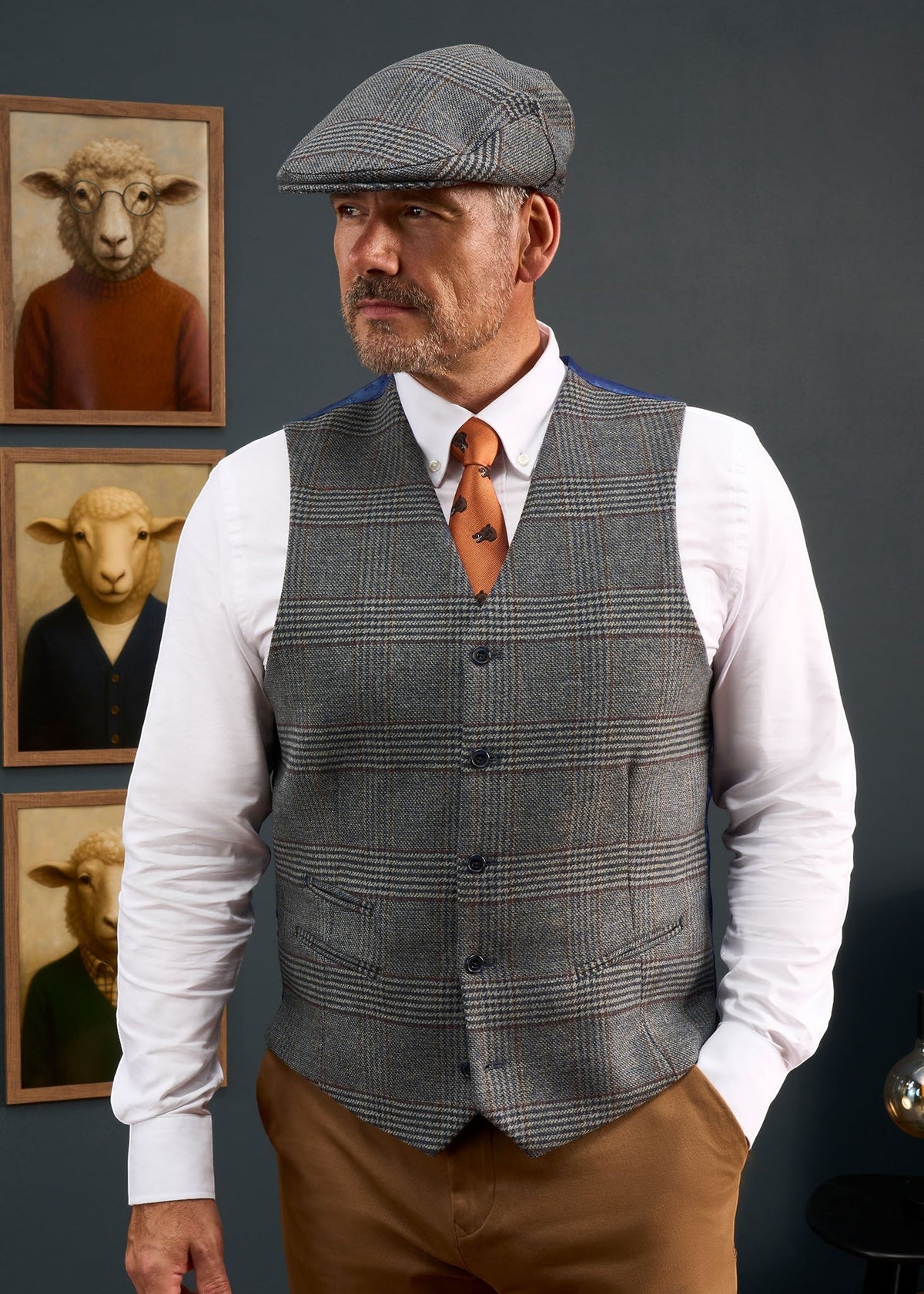 A man wears a Surrey Men’s Tweed Water Repellent Lined Waistcoat in Blue Check, white shirt, orange tie, and matching cap.