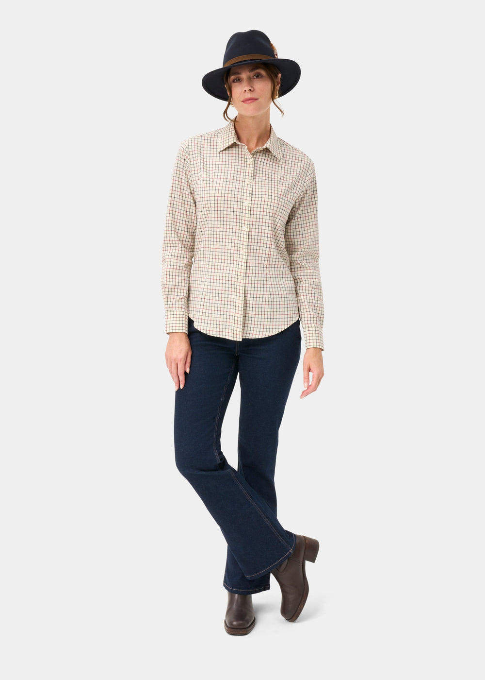 Woman wears Bromford Ladies Cotton Shirt In Red Check, dark jeans, boots, black hat against a white background.