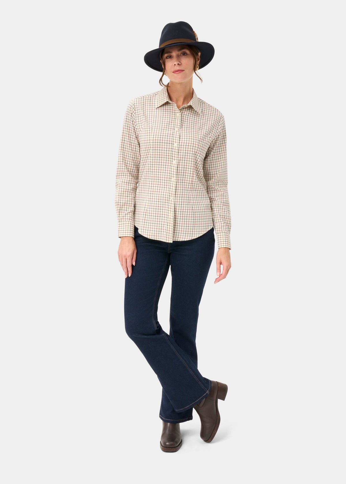 Woman wears Bromford Ladies Cotton Shirt In Red Check, dark jeans, boots, black hat against a white background.