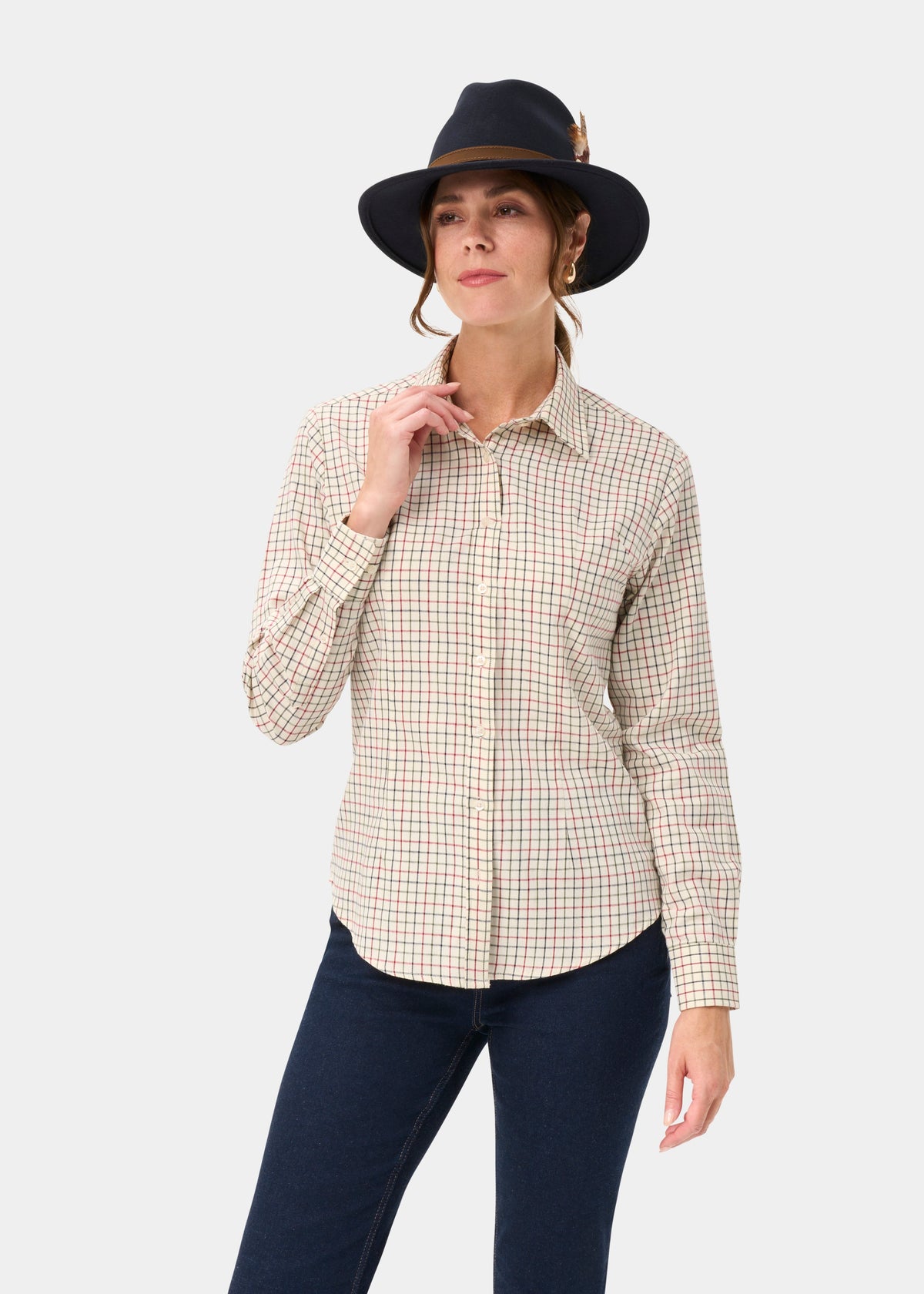 Woman in Bromford Ladies Cotton Shirt In Red Check poses with a dark hat, one hand near collar, on white background.
