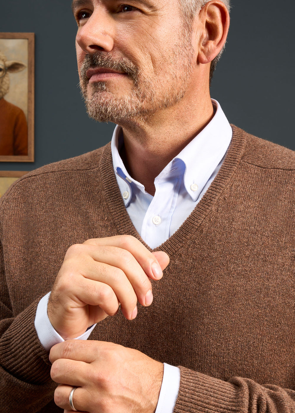 Man in Hampshire Lambswool Vee Neck Jumper In Tobacco adjusts cuff, with beard, ring, white shirt visible.