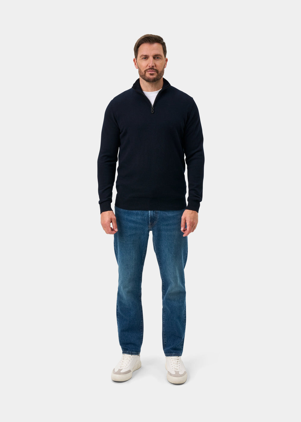 Man in Hanbury Pure Cashmere Quarter Zip Jumper in dark navy, blue jeans, and white sneakers on a plain background.