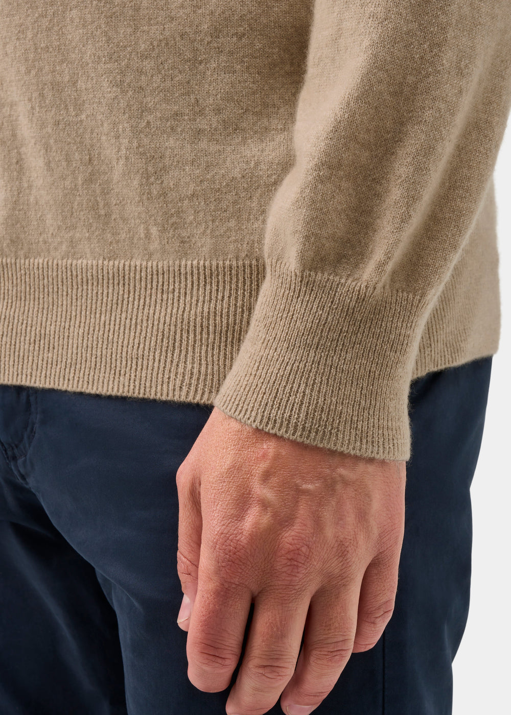 A person wears the Haddington Pure Cashmere V-Neck Jumper in Linen with dark pants, hand at their side, waist down.