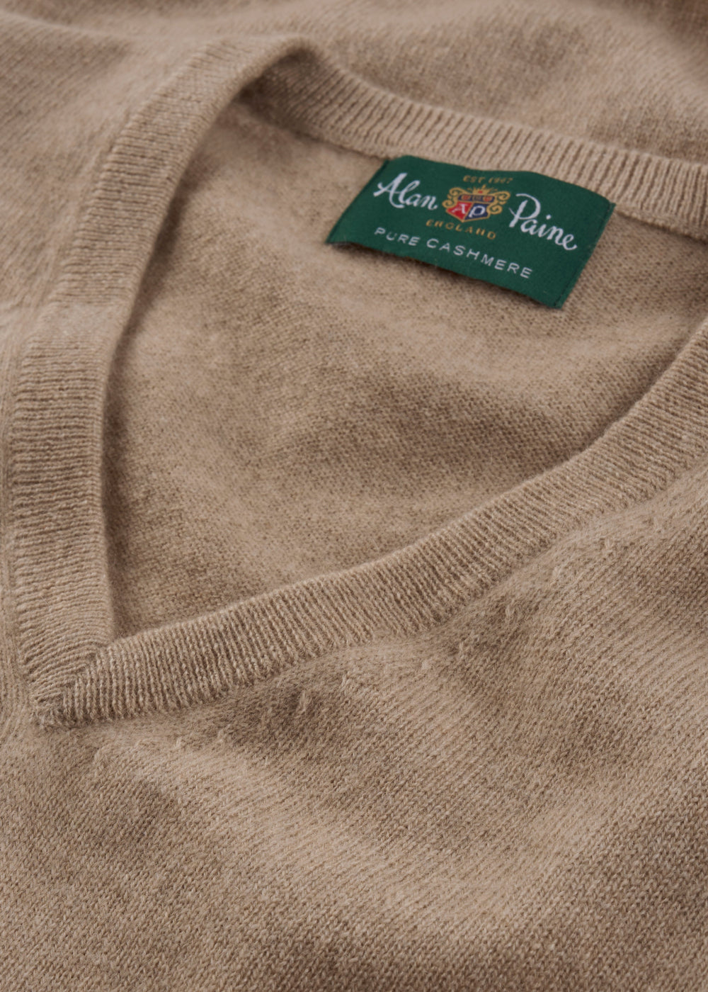 Close-up of a beige Haddington Pure Cashmere V-Neck Jumper In Linen, regular fit with green label.