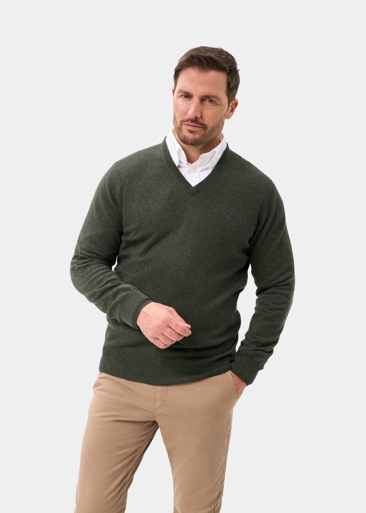 Man in a Haddington Pure Cashmere V-Neck Jumper in Rosemary and khaki pants stands with one hand in his pocket.