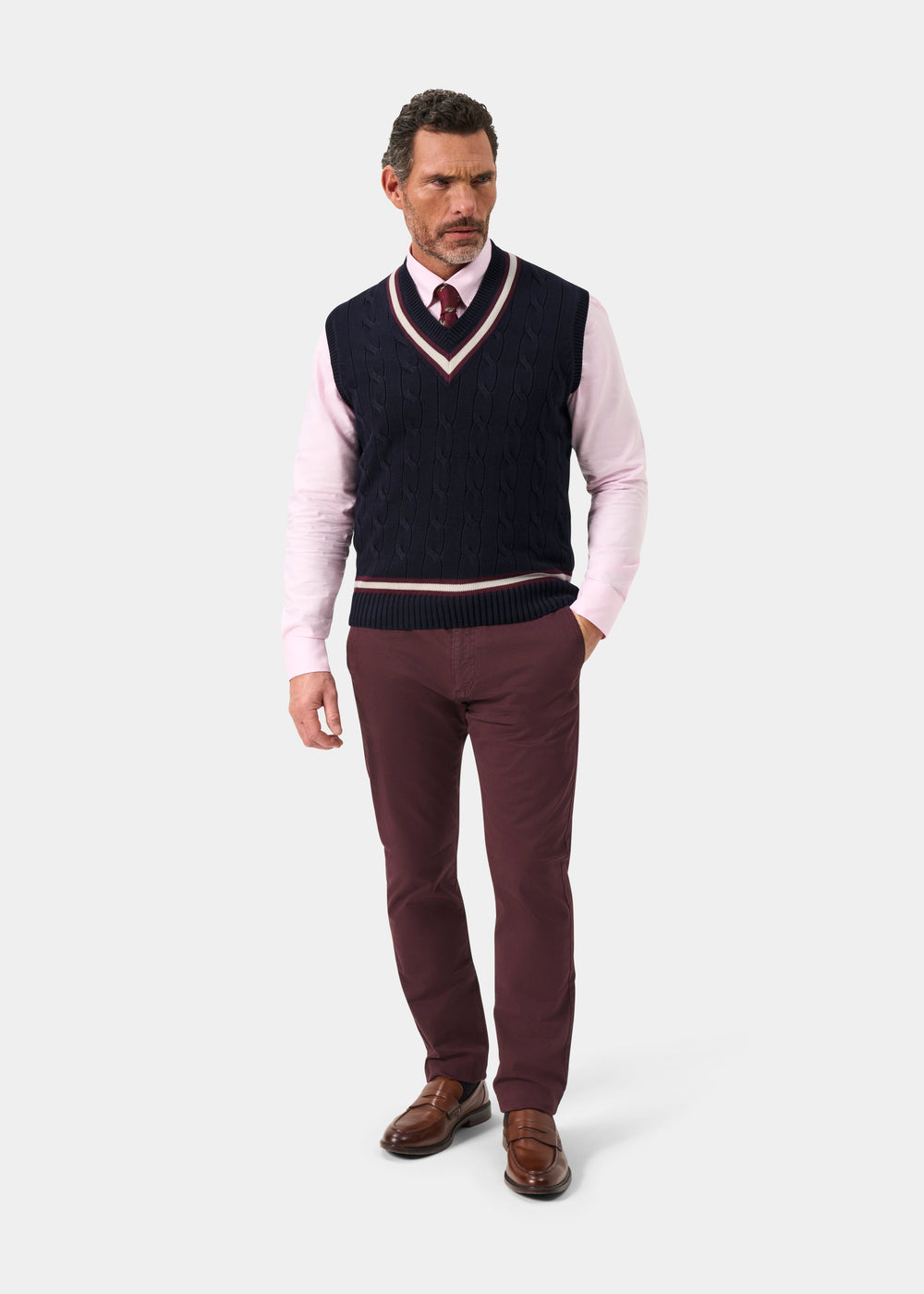 Man in Chadbury V-neck cricket slipover, pink shirt, burgundy tie and pants, brown shoes; on white background.