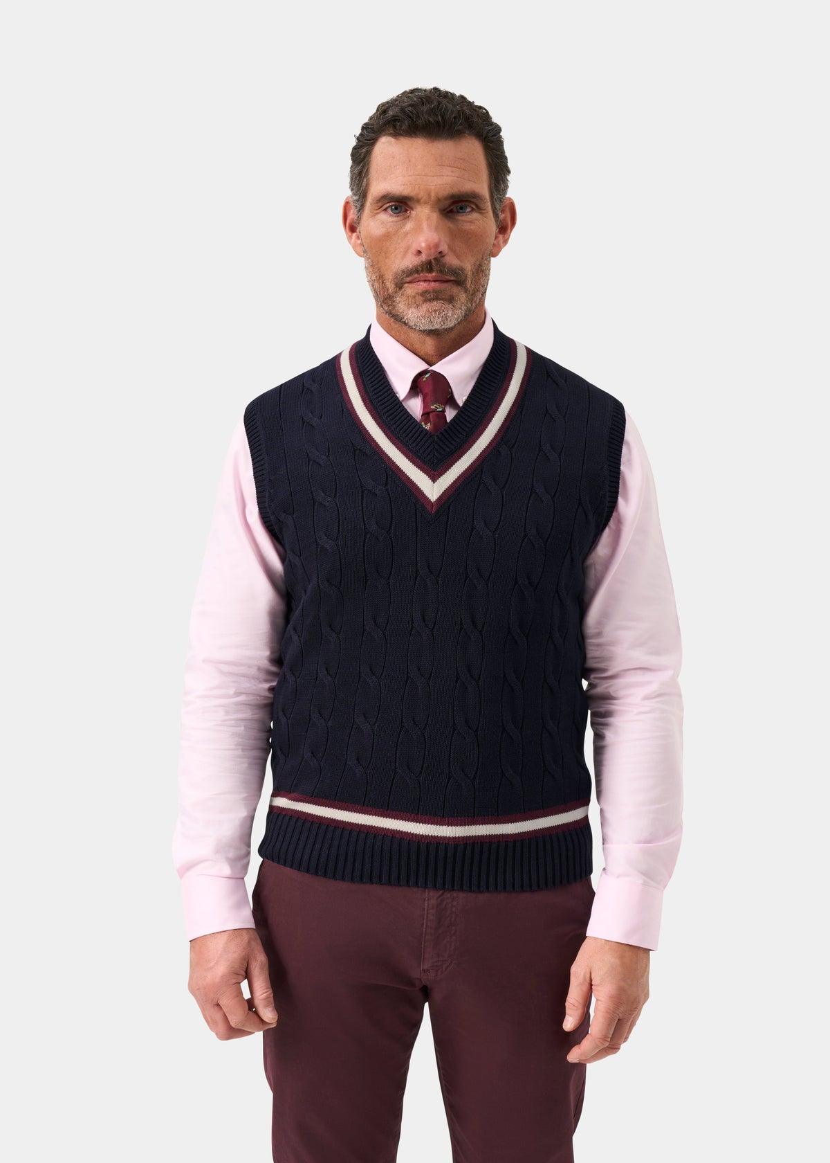 Man in Chadbury navy cricket slipover, pink shirt, burgundy tie, maroon pants, on white background.