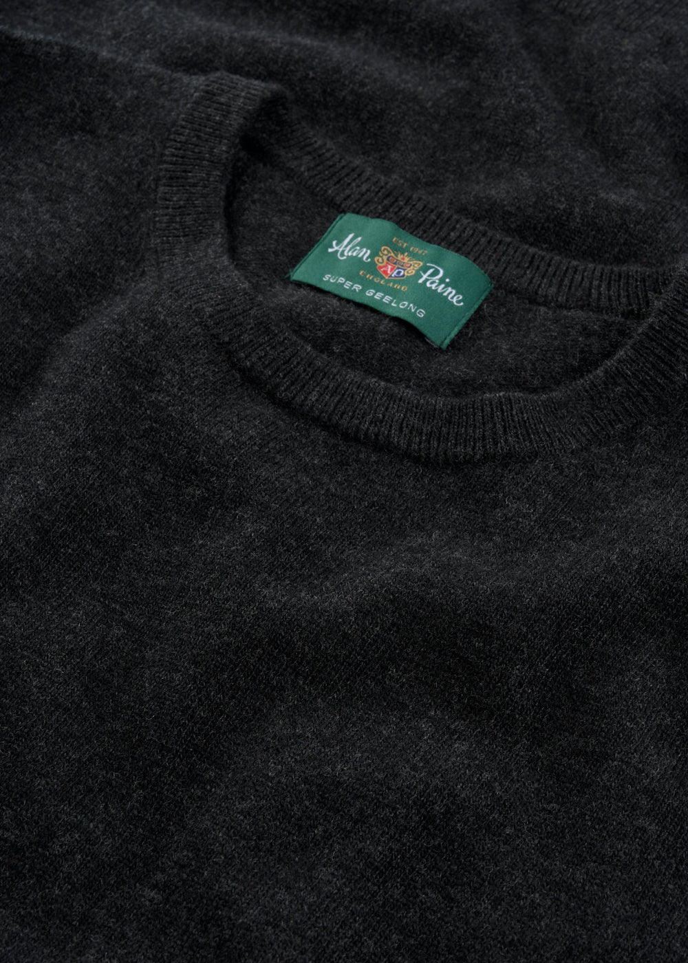 Close-up of the Brisbane Geelong Wool Crew Neck Jumper in Charcoal - Regular Fit, featuring a green Super Geelong label.