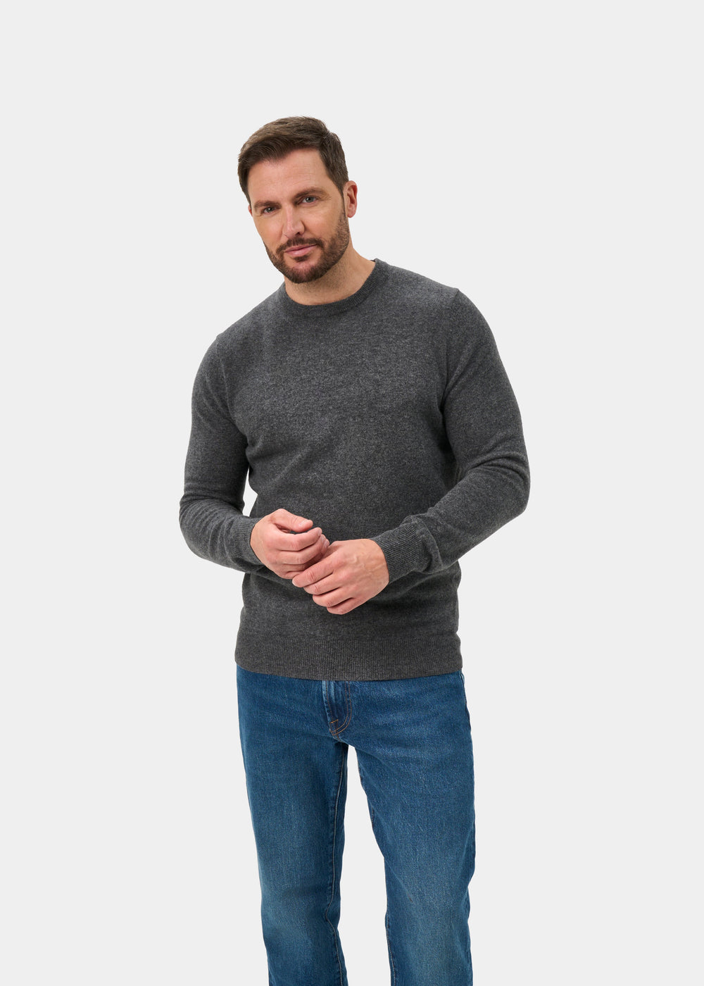 Man wears Brisbane Geelong Wool Crew Neck Jumper in Derby, regular fit, with blue jeans against a white background.