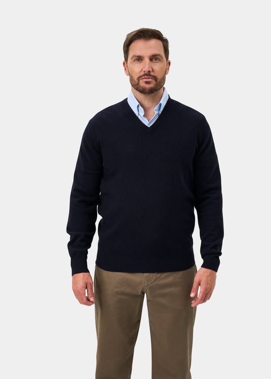A man in an Albury Geelong Wool V-Neck Jumper in dark navy stands against a plain white background.