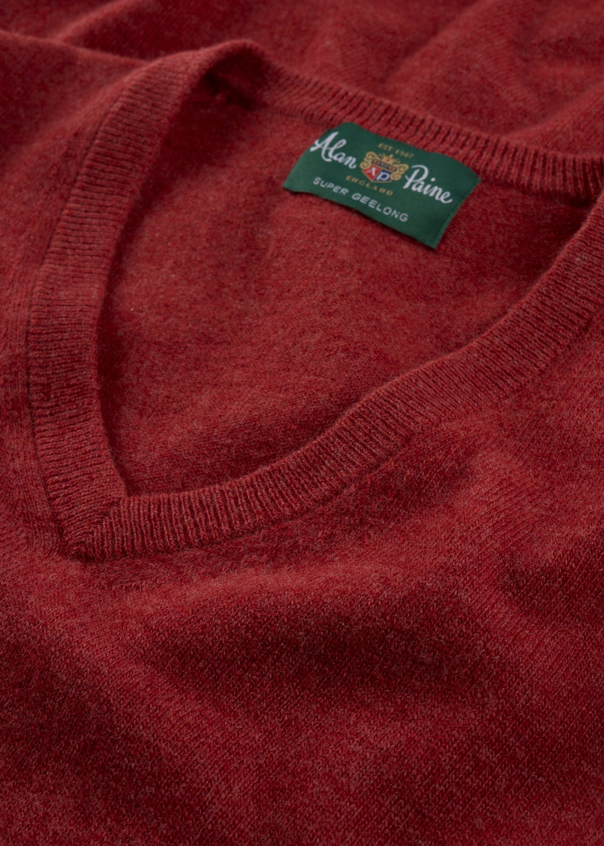 A close-up of the Albury Geelong Wool V-Neck Jumper in Poppy Melange with a green label at the neck.