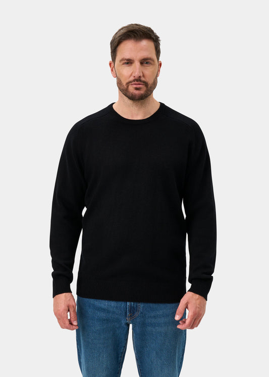Bearded man with short brown hair wears Dorset Lambswool Crew Neck Jumper in Black, classic fit, and blue jeans.
