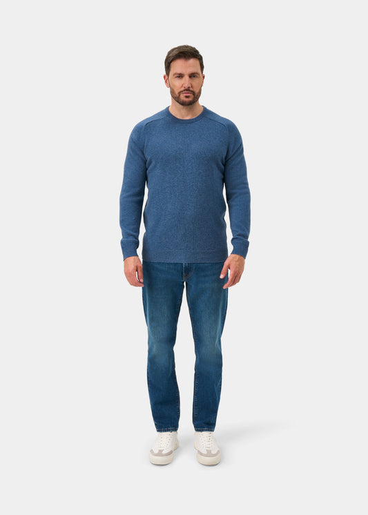 Man in a Lenzie Lambswool Crew Neck Jumper in Jeans - Regular Fit, blue jeans, and white sneakers on a white background.