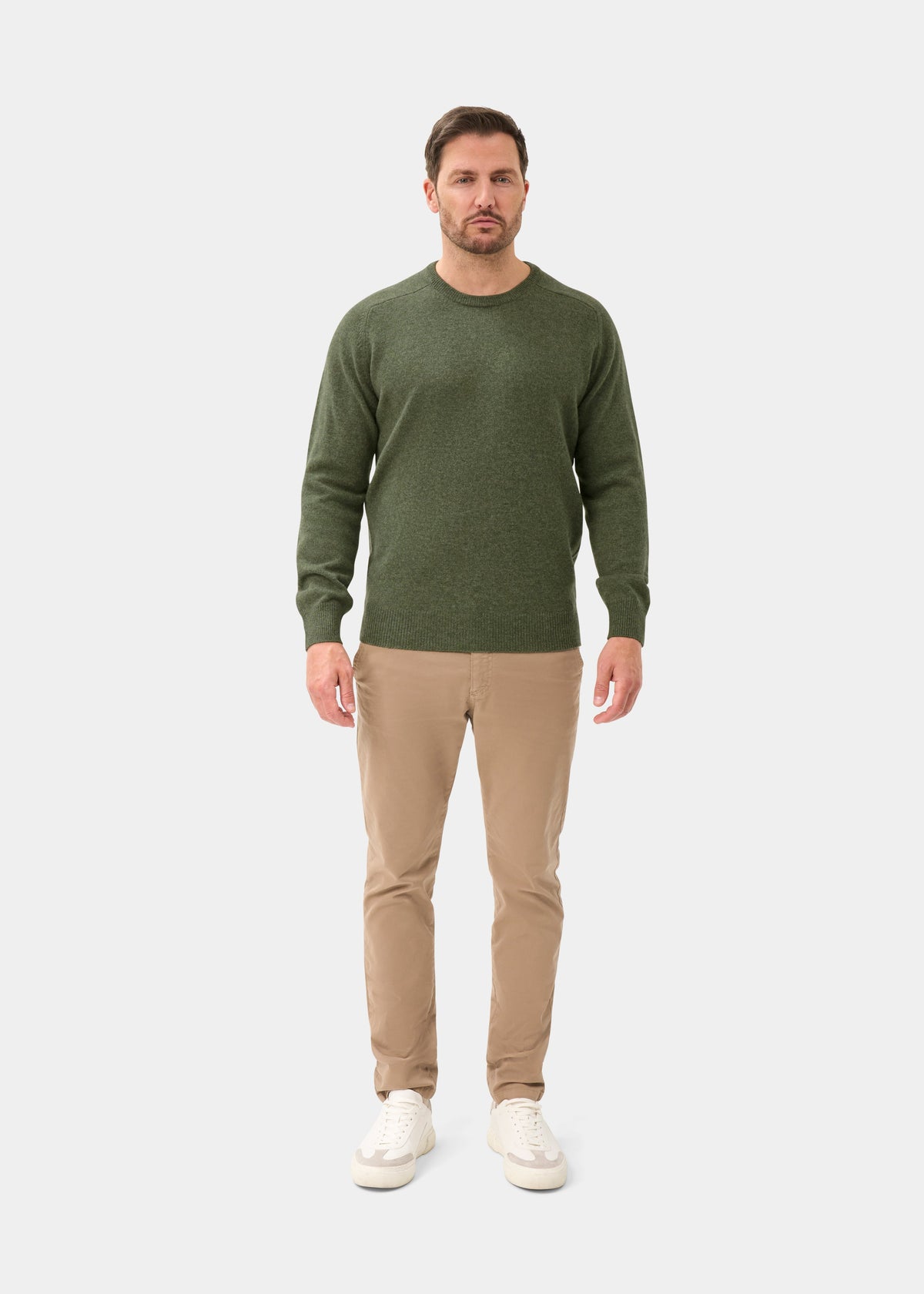 Man in a Dorset Lambswool Crew Neck Jumper in Landscape, beige pants, and white sneakers stands before a plain background.