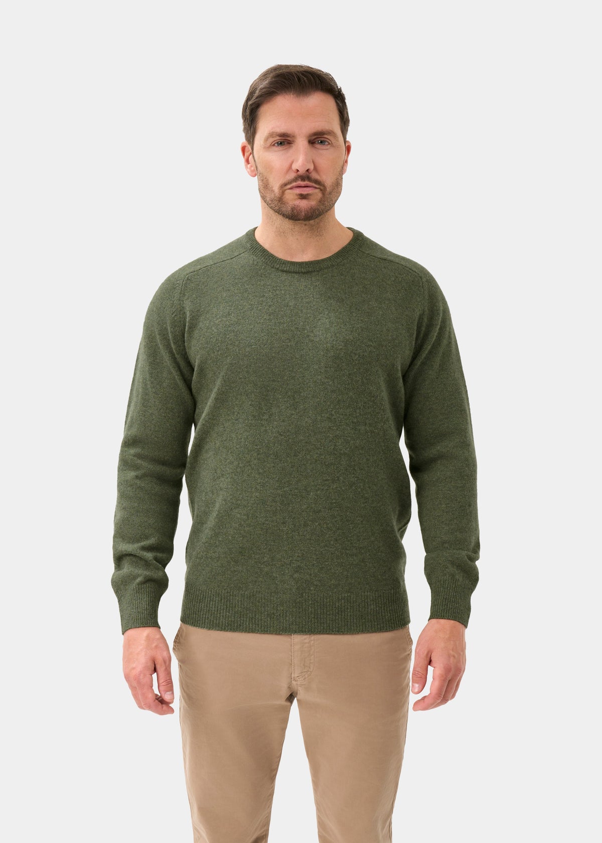Man in Dorset Lambswool Crew Neck Jumper in Landscape, classic fit, with beige pants stands against white background.