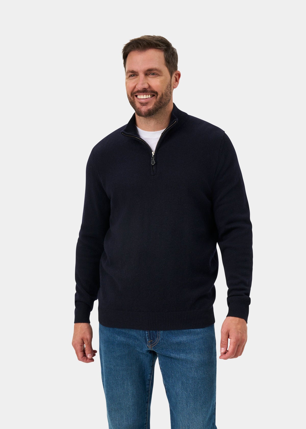 A man wears a navy Sutherland Lambswool Quarter Zip Jumper over a white t-shirt and blue jeans.