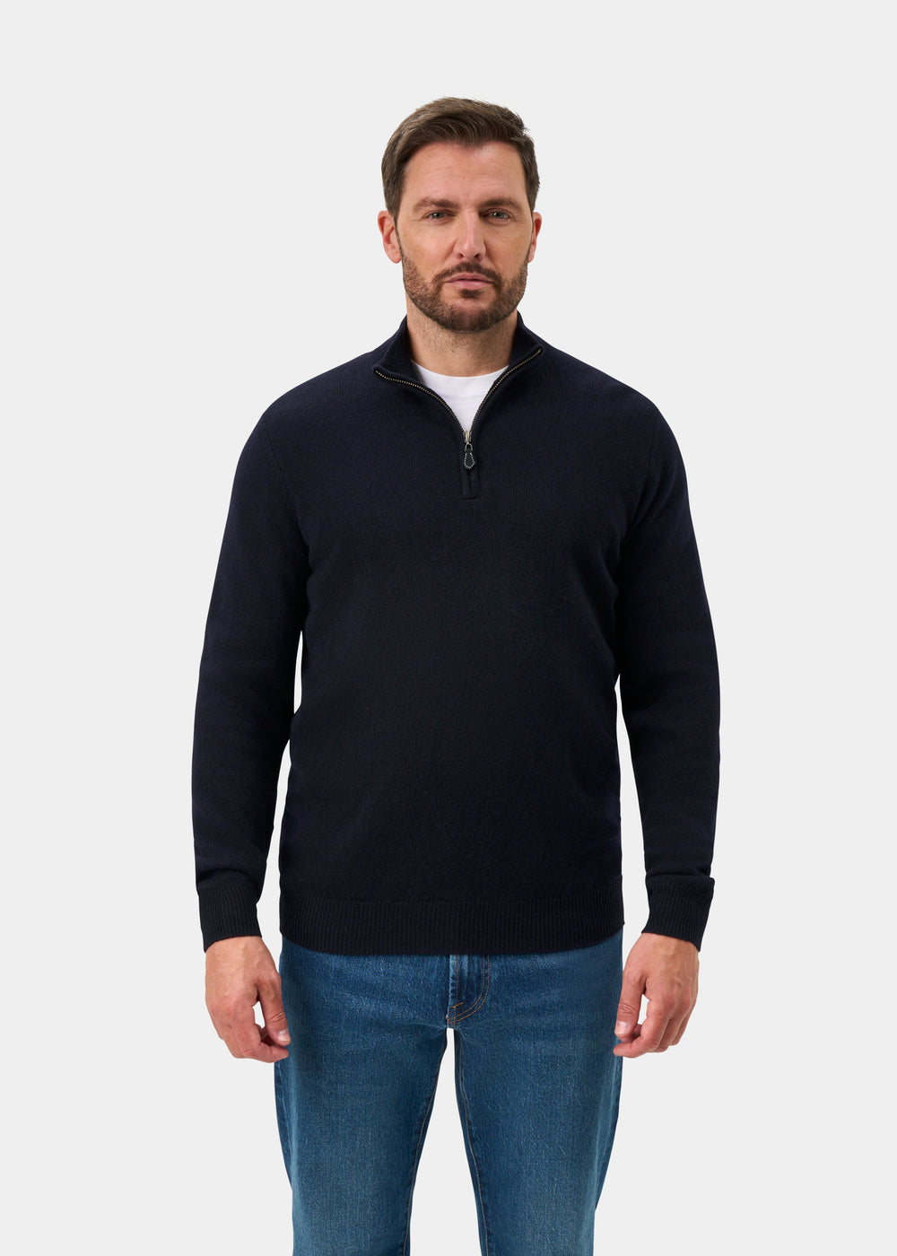 A man wearing a Sutherland Lambswool Quarter Zip Jumper In Navy over a white t-shirt and blue jeans.