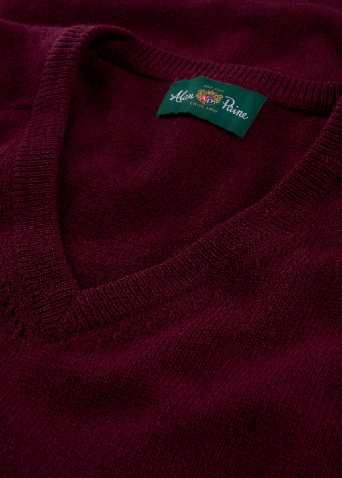 Close-up of the Kilsyth Lambswool V-Neck Jumper in Bordeaux, showing the Alan Paine label inside the collar.