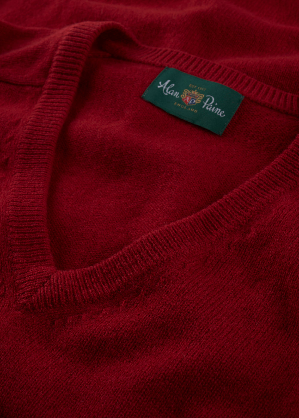 Close-up of the Hampshire Lambswool Vee Neck Jumper in Dubonnet, classic fit, with green Alan Paine collar label.