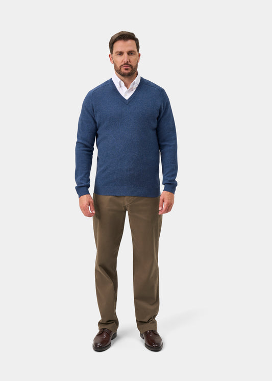 Man in Kilsyth Lambswool Vee Neck Jumper In Jeans, white shirt, khaki pants, and brown shoes stands against plain background.