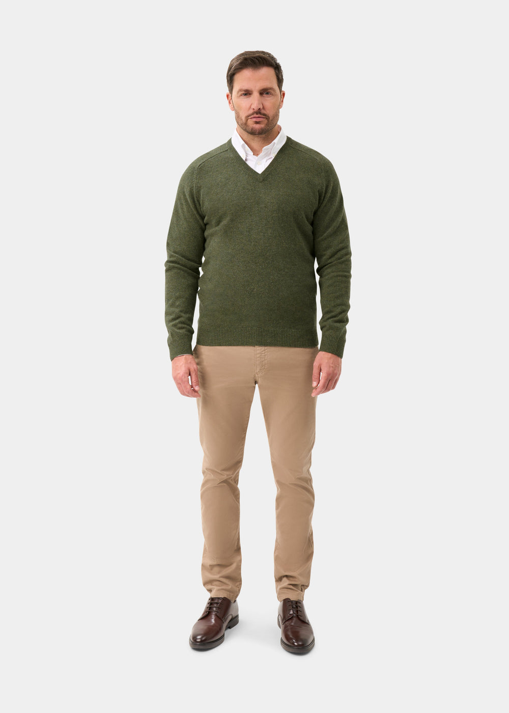 Man wearing Kilsyth Lambswool V-Neck Jumper in Landscape, white shirt, beige pants, brown shoes on white background.