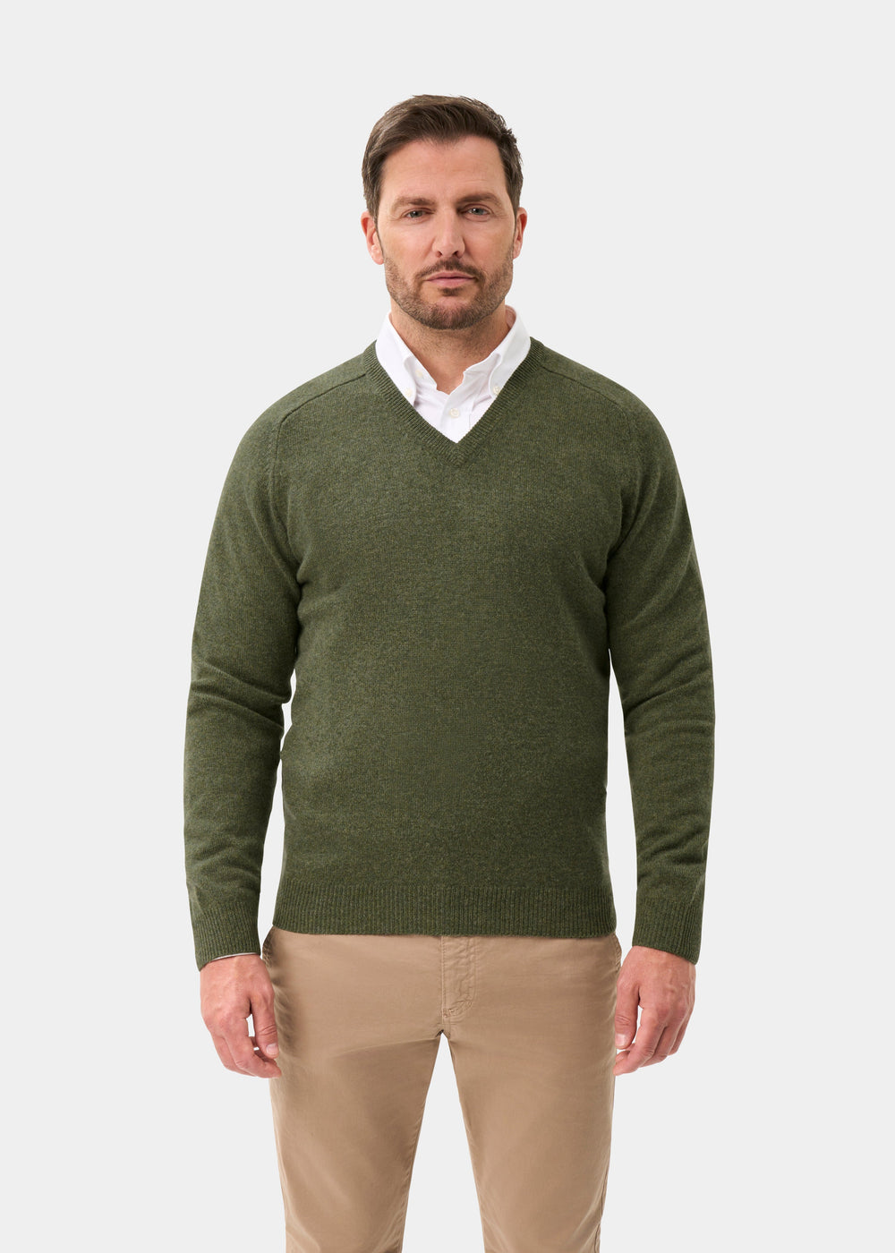 Man in Kilsyth Lambswool V-Neck Jumper in Landscape, white shirt, beige pants stands against plain background.