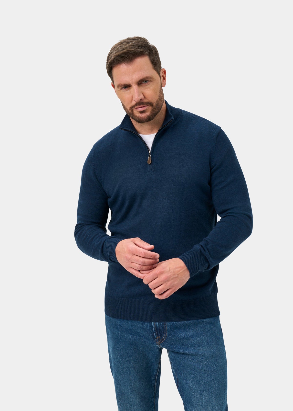 Man wears the Barton Merino Wool Quarter Zip Jumper in Indigo, regular fit, with blue jeans against a light gray backdrop.