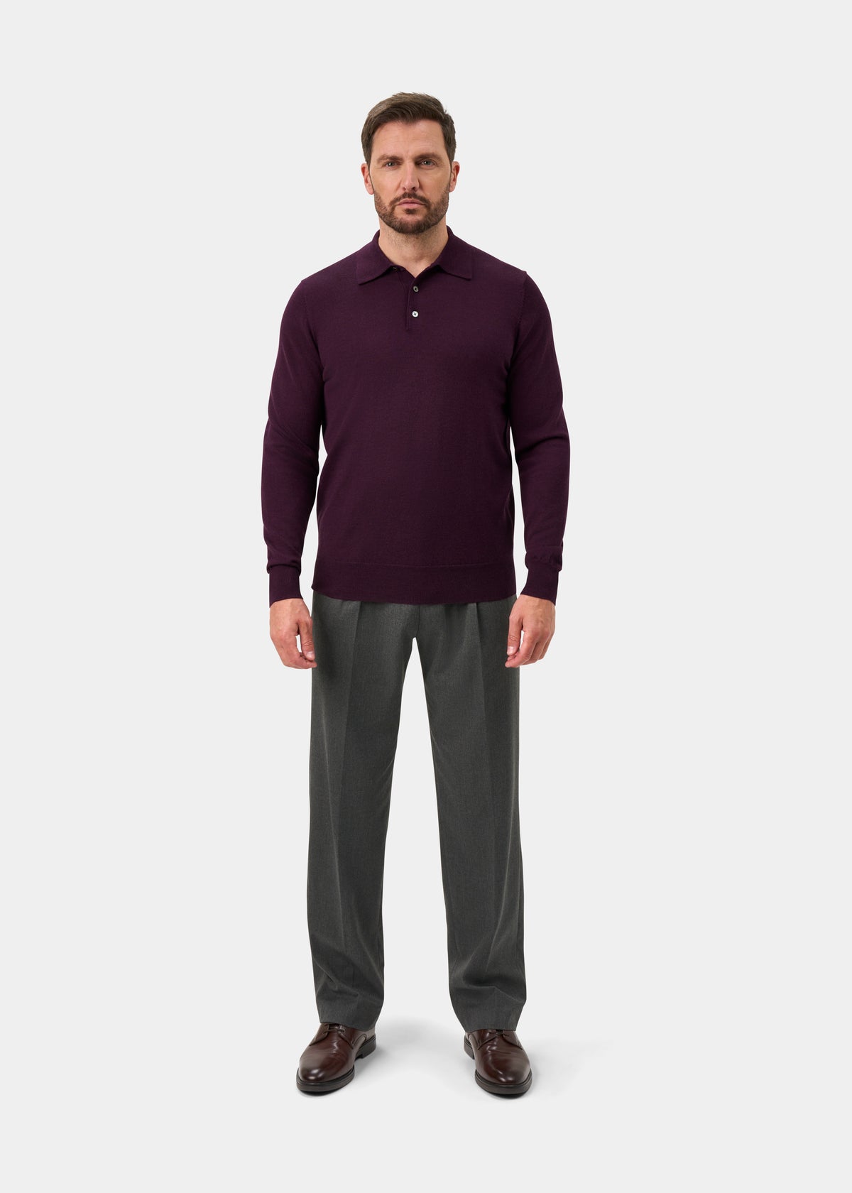 Man wearing Hindhead Men’s Merino Wool Polo Shirt in Black Grape, gray trousers, brown shoes, on a white background.