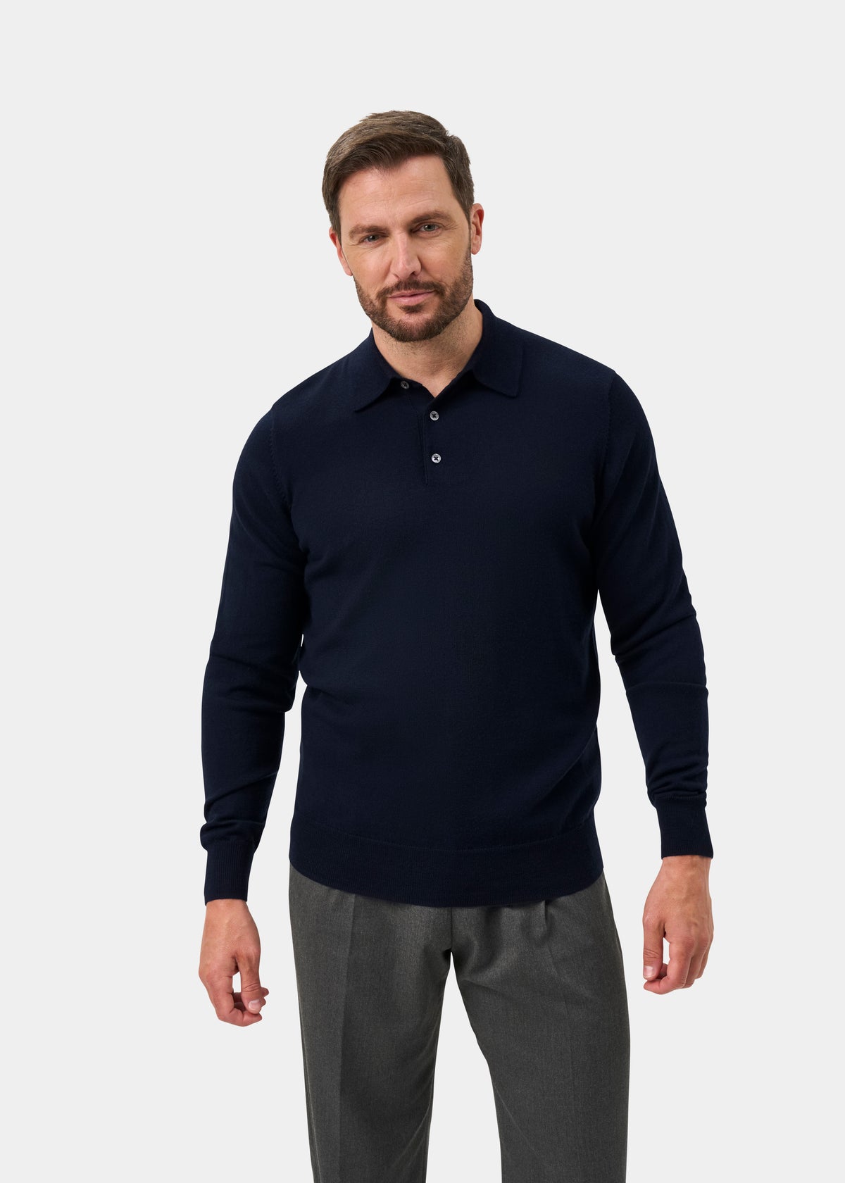 Man in Hindhead Men’s Merino Wool Polo Shirt, Dark Navy, Regular Fit, and gray trousers against a white background.
