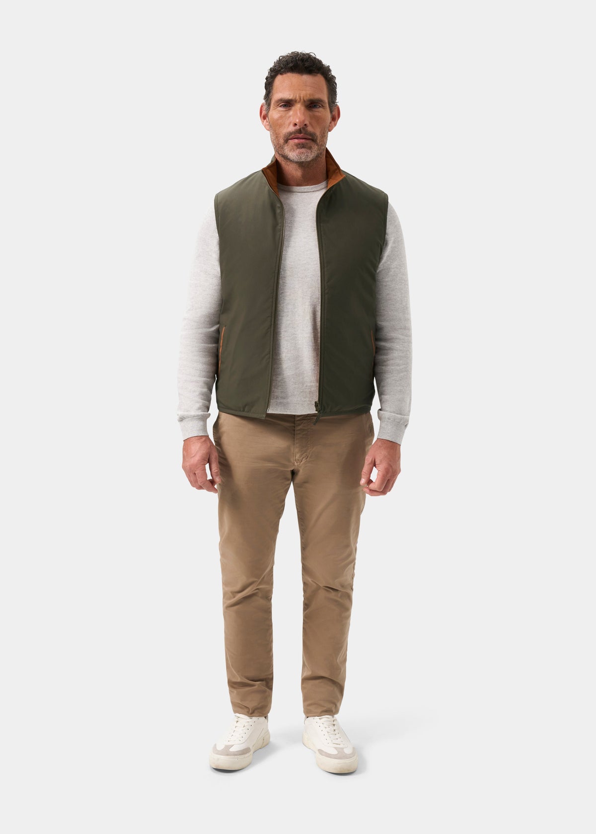 Man wearing a Swifthall Reversible City Gilet In Olive and Cider over a grey long-sleeve shirt and khaki trousers.