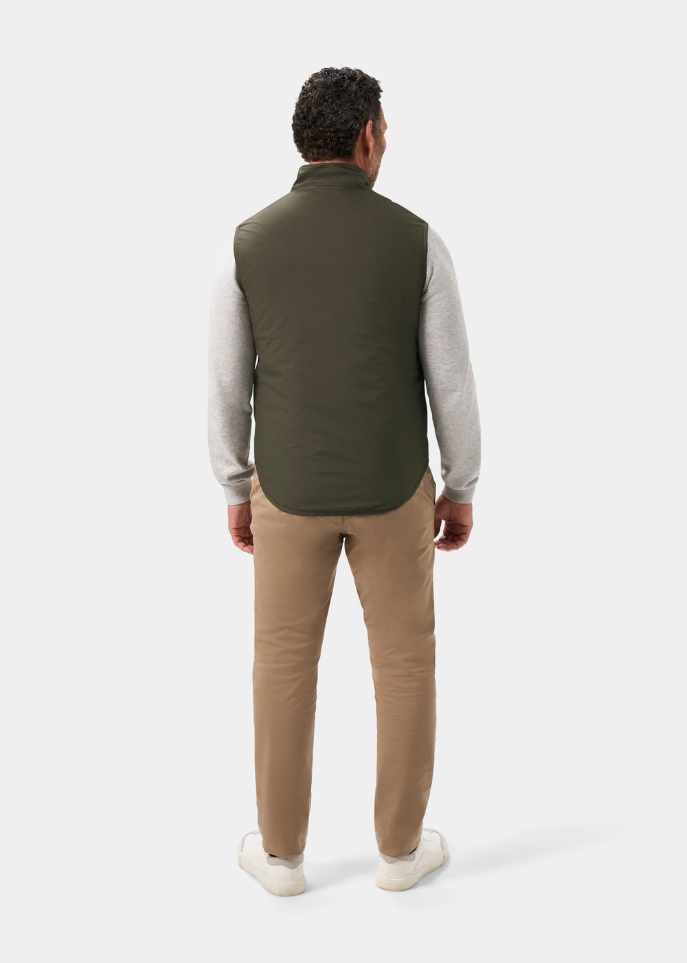 Back view of a person wearing a Swifthall Reversible City Gilet In Olive and Cider over a gray sweater and tan trousers.