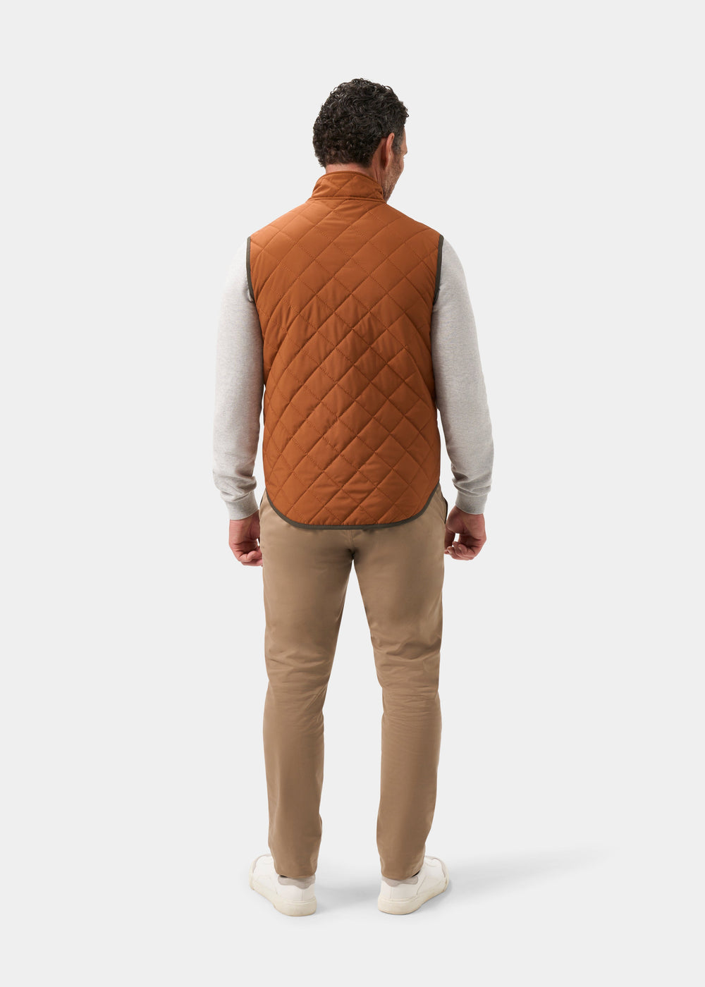 Back view of a person wearing a Swifthall Reversible City Gilet In Olive and Cider over a grey shirt and tan trousers.