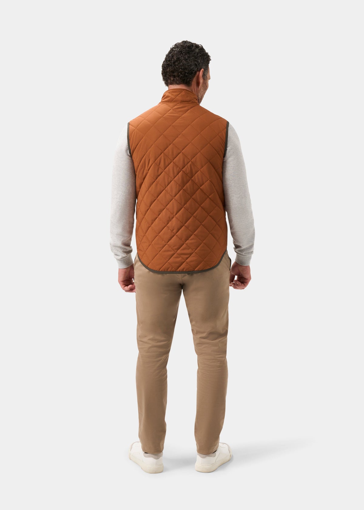 Back view of a person wearing a Swifthall Reversible City Gilet In Olive and Cider over a grey shirt and tan trousers.