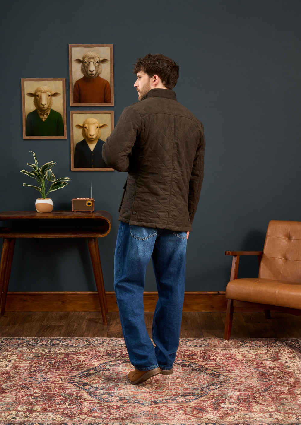 Man in an olive Felwell Children’s Quilted Jacket stands in a vintage room with animal portraits and retro furniture.