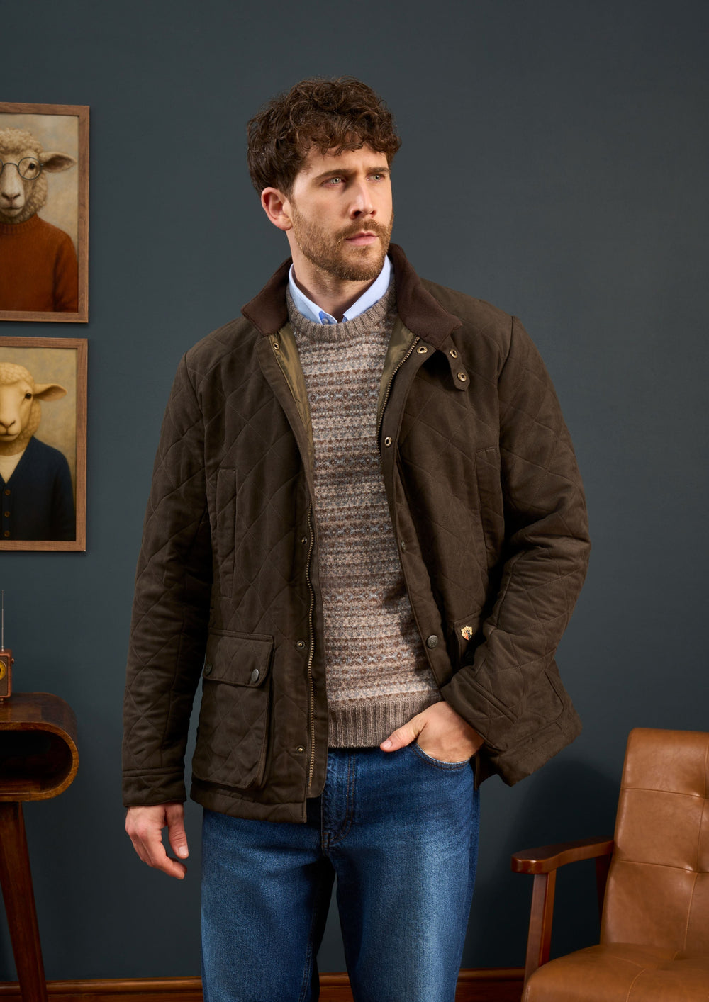 A boy in a Felwell Children’s Quilted Jacket in Olive stands indoors near a chair and animal portraits on a dark wall.