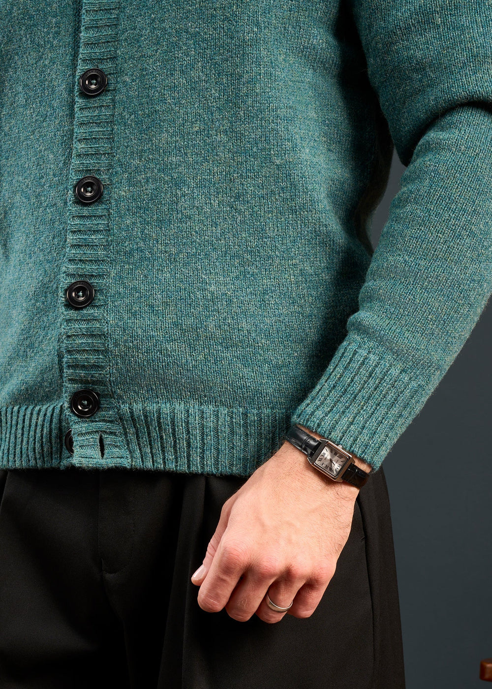Model in Kinloch Supersoft Shetland Wool V-Neck Cardigan in Kingfisher, black pants, and watch; hand at side.