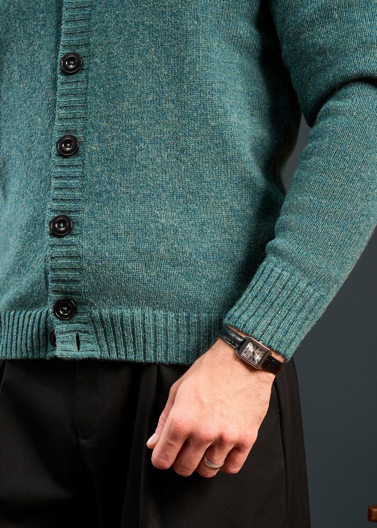 Model in Kinloch Supersoft Shetland Wool V-Neck Cardigan in Kingfisher, black pants, and watch; hand at side.