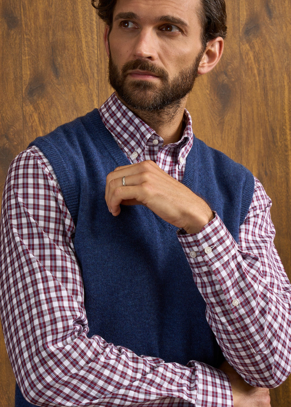 A man wears a Norfolk Lambswool V-Neck Slipover In Rhapsody over a red and white plaid button-down shirt.