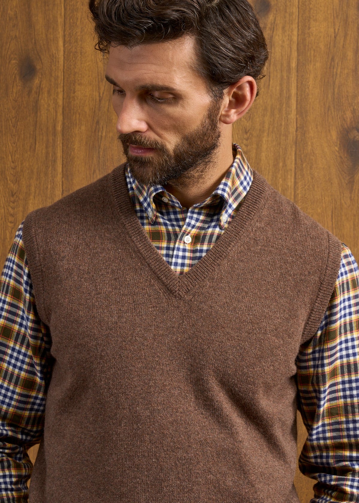 A man wearing a Norfolk Lambswool V-Neck Slipover In Tobacco over a plaid button-down shirt.