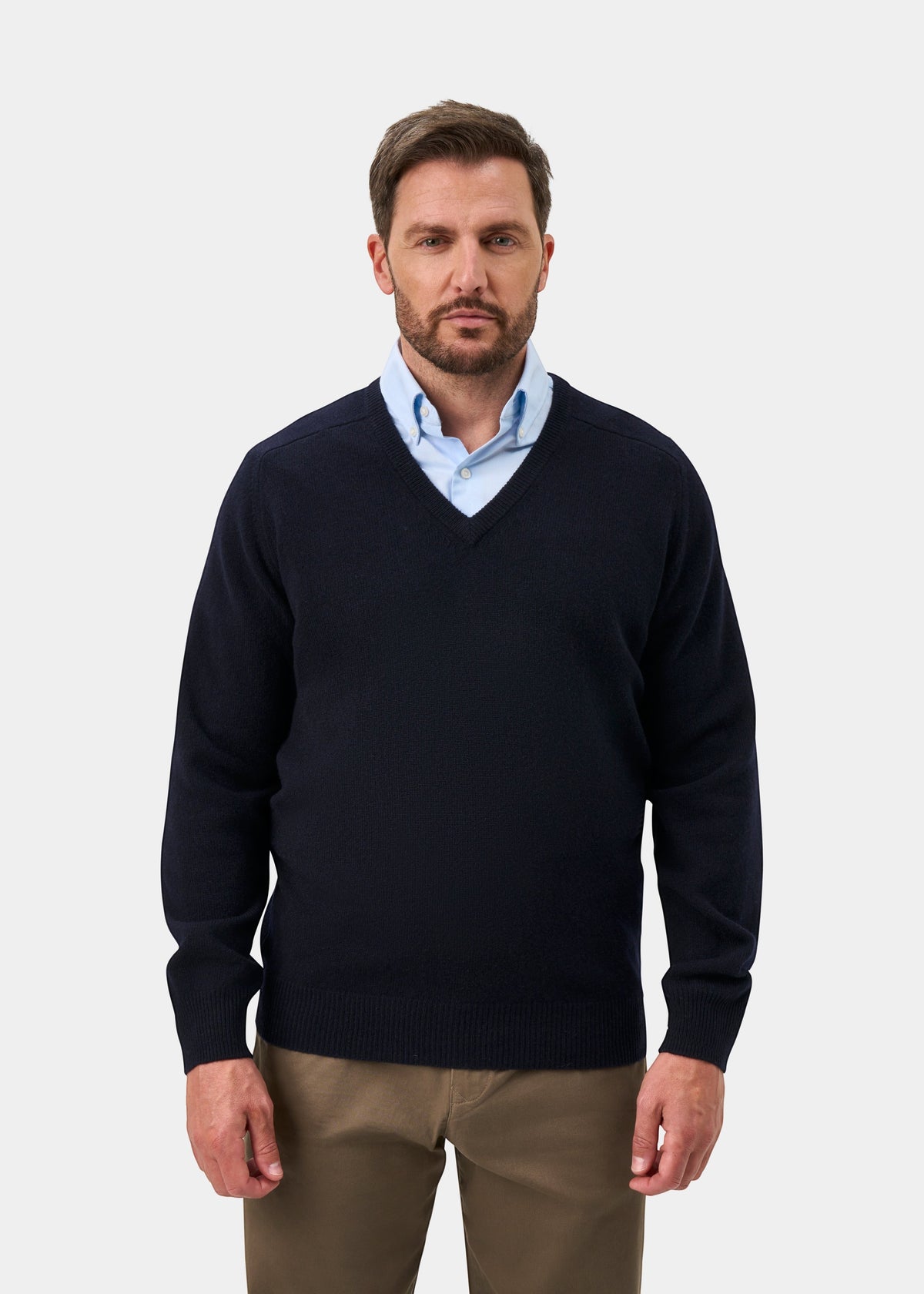 Man in Hampshire Lambswool V-Neck Jumper in Navy, light blue shirt, and khaki pants against a plain background.