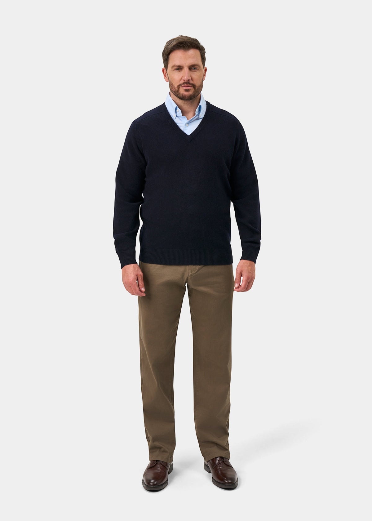 Man in Hampshire Lambswool V-Neck Jumper, navy, with a blue shirt, khaki pants, and brown shoes on white background.