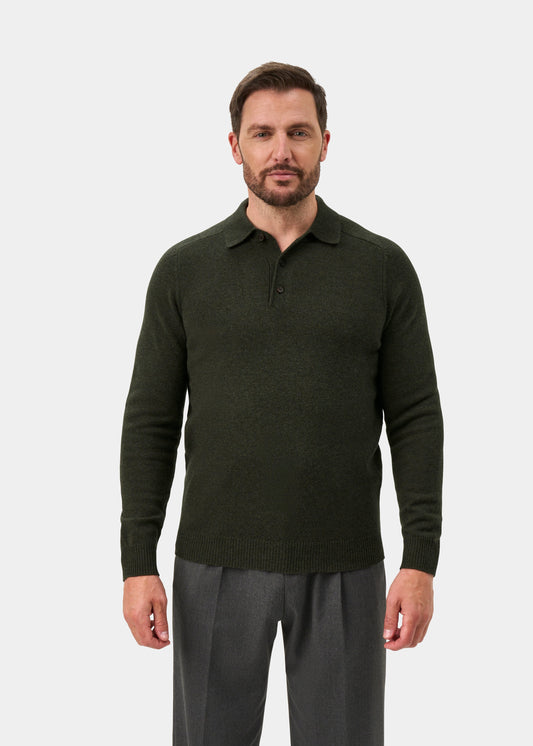 Man wears Bilsdean Men’s Lambswool Long Sleeve Polo in Seaweed, styled with gray pants against a plain light backdrop.