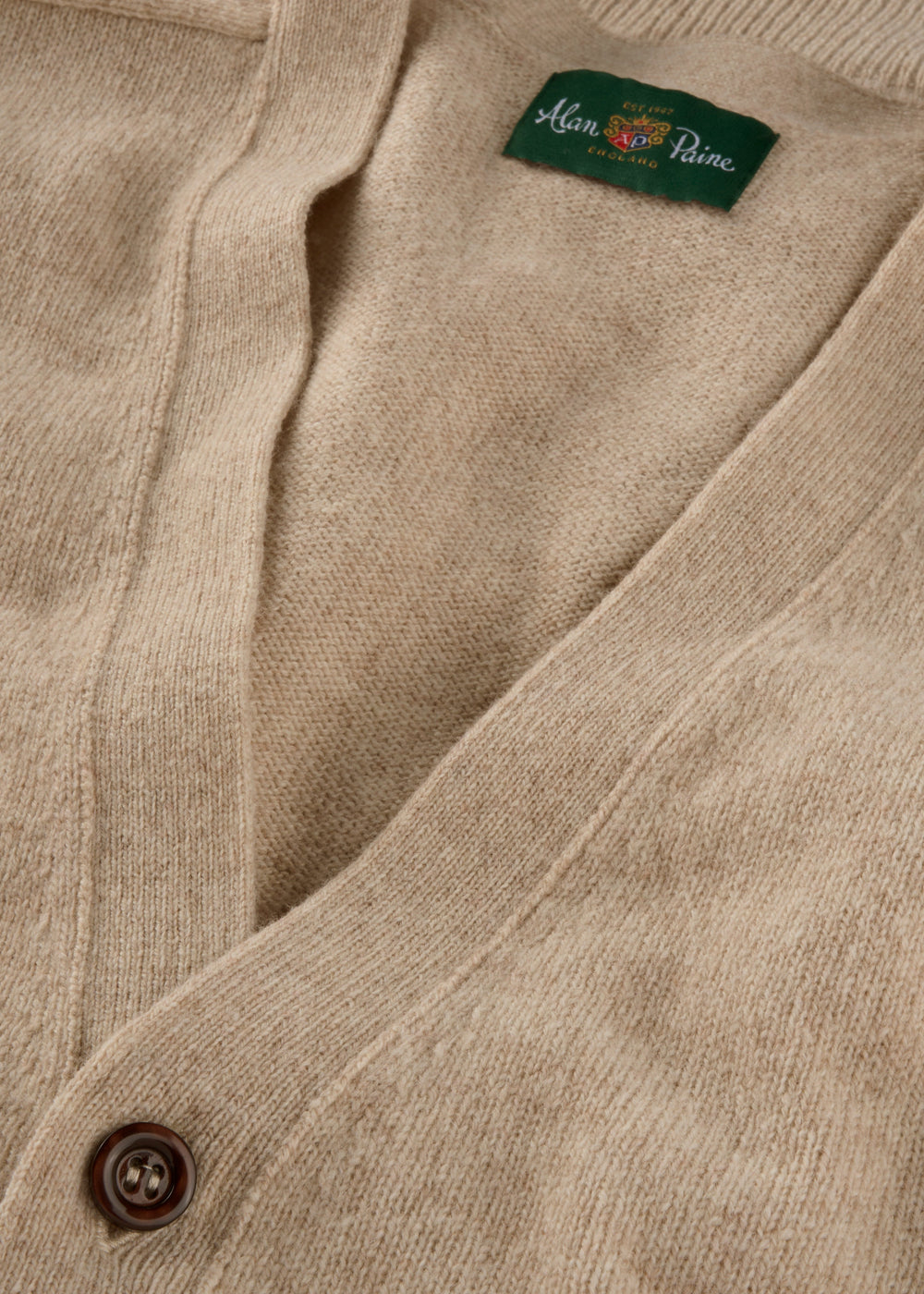 Close-up of the Cornwall Lambswool V-Neck Cardigan in Linen, Classic Fit, with button and green Alan Paine label.