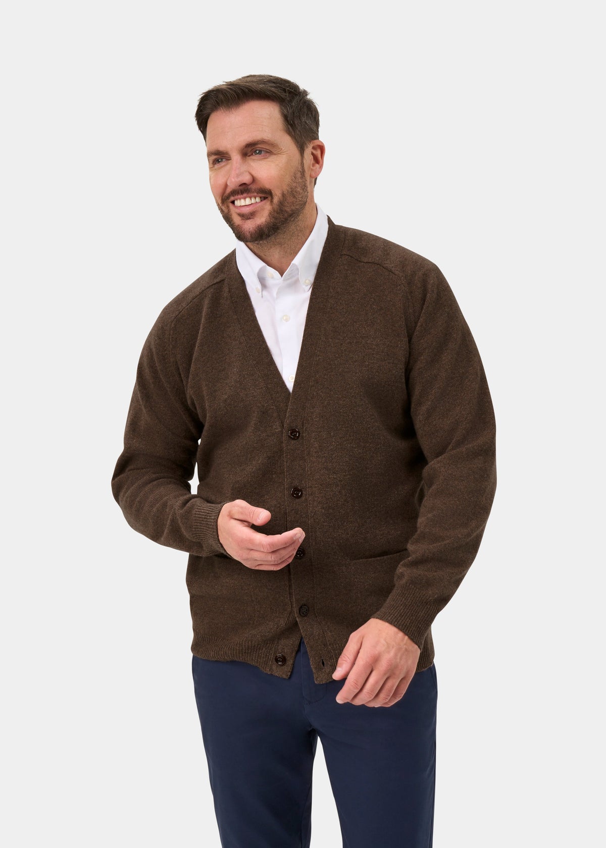 Man in Cornwall Lambswool V-Neck Cardigan in Tobacco, classic fit, over white shirt, smiles against light gray background.