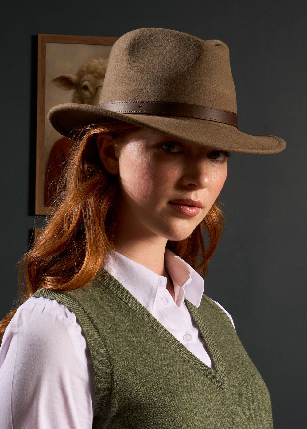 Woman with long red hair wears the Erin Wool & Cashmere V-Neck Slipover in Landscape, standing near framed animal art.