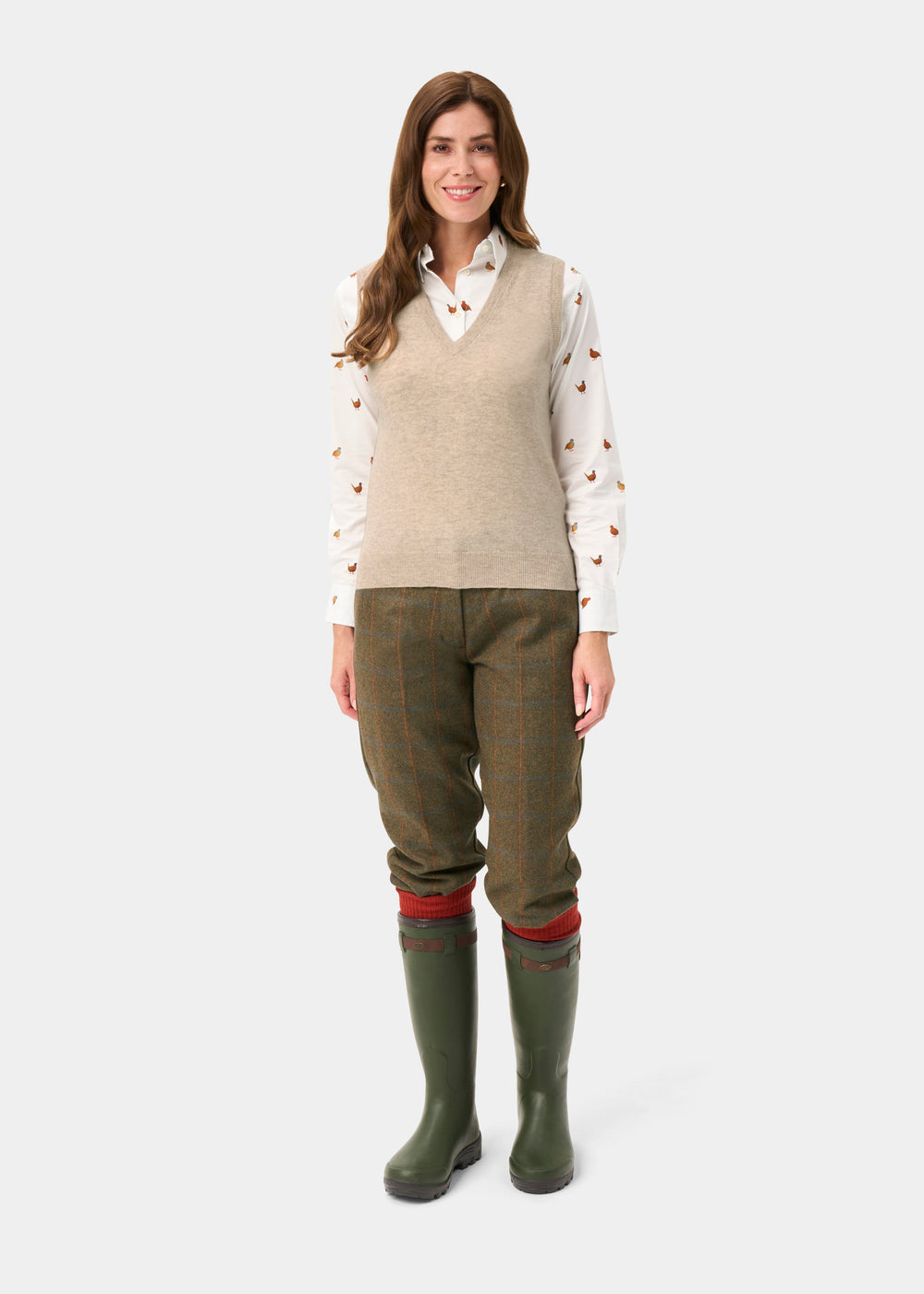 Woman wears Erin Wool & Cashmere V-Neck Slipover in Porridge, patterned shirt, tweed pants, and green rain boots.