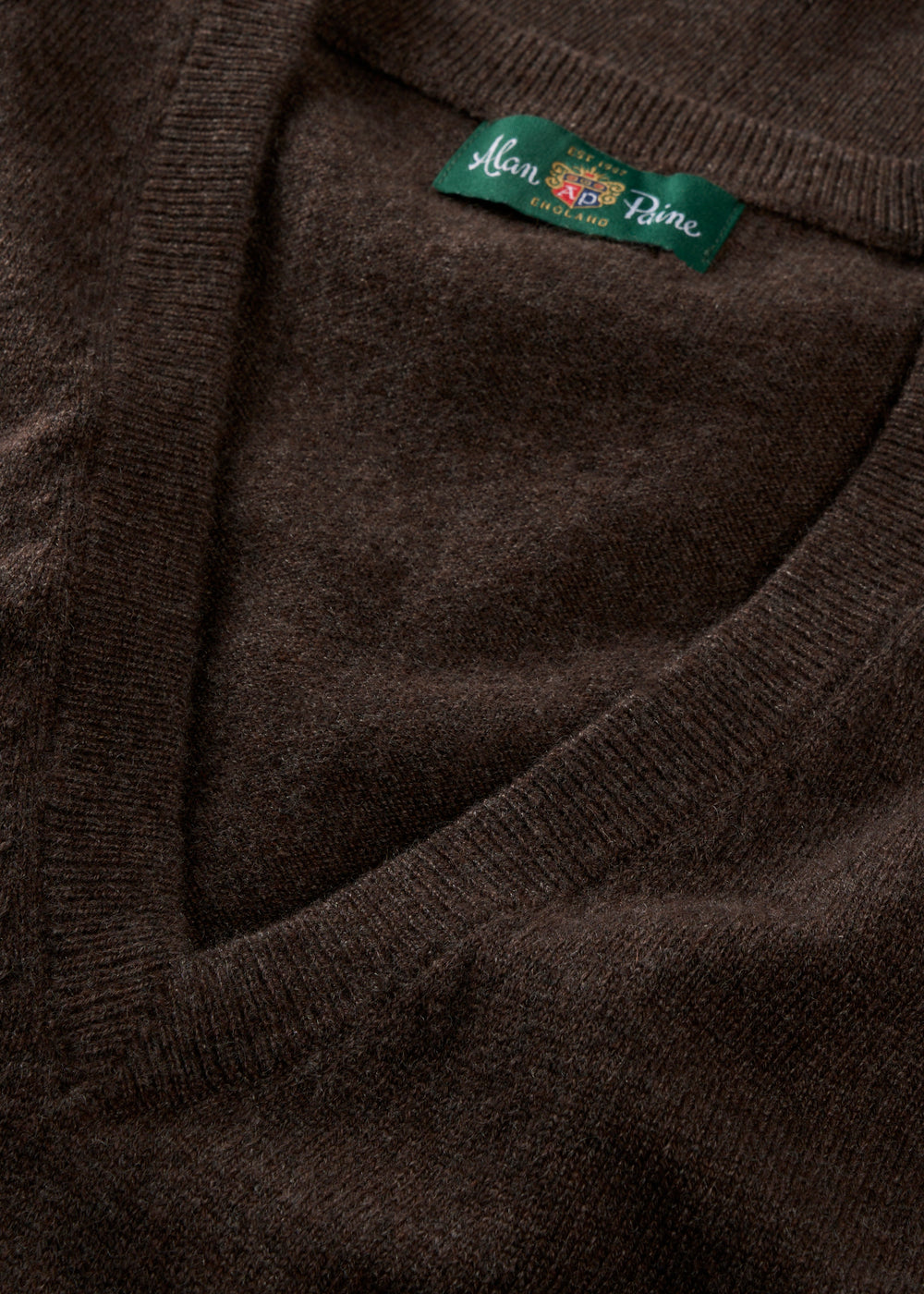 Close-up of the Erin Wool & Cashmere V-Neck Slipover in Walnut with a green label on a soft, textured backdrop.