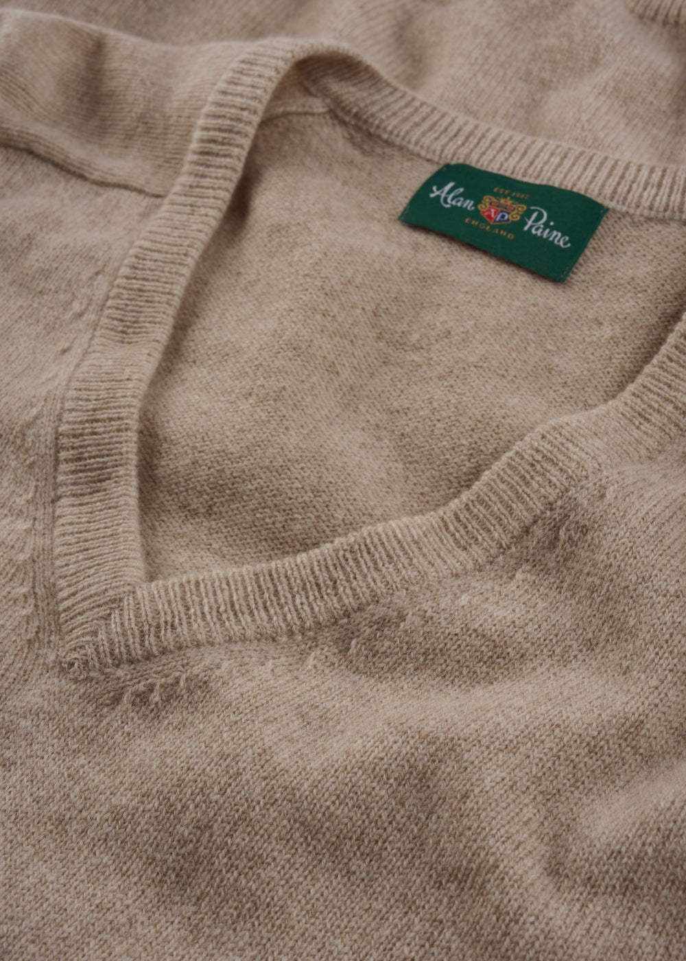A close-up of the Hampshire Lambswool V-Neck Jumper in Linen (Classic Fit) with green branded label.