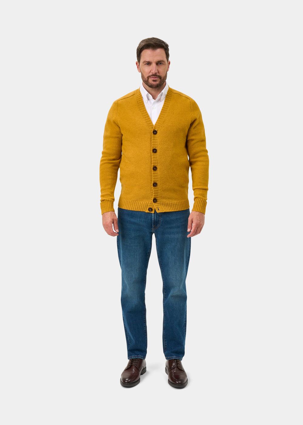 Man in Kinloch Supersoft Shetland Wool V-Neck Cardigan in Old Gold, white shirt, blue jeans, and brown shoes.